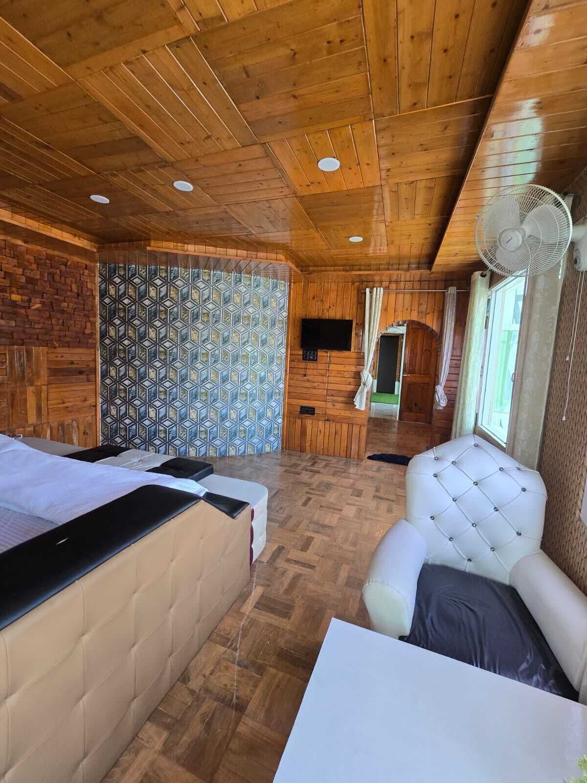 A wooden cabin interior with a bed, a seating area, and a television.