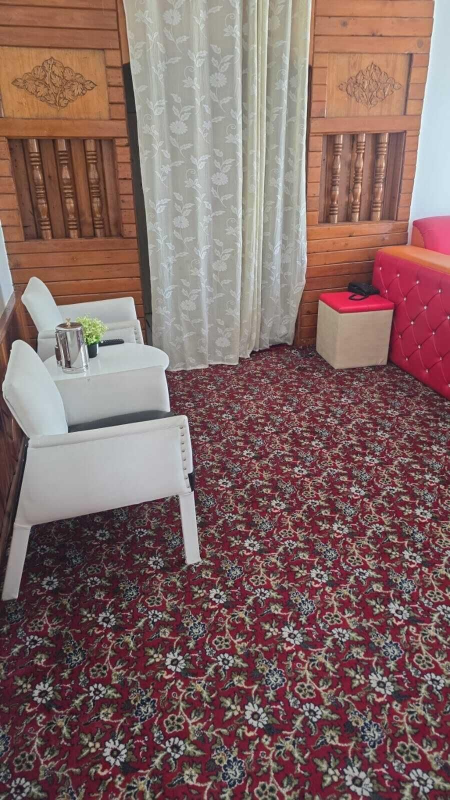 A room with a red patterned carpet, a white armchair, a red sofa, and a small table with a plant.