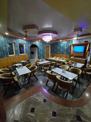 Un salón de conferencias con mesas y sillas, una lámpara de araña y una pantalla de televisión.
