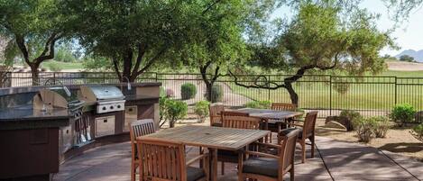 An outdoor patio with a grill, wooden furniture, and a view of a grassy area.
