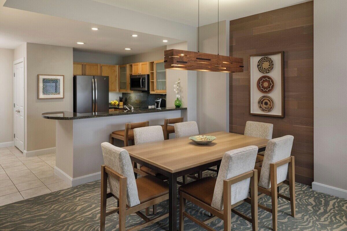 A modern kitchen with a central island, wooden chairs, and a dining table.