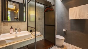 Casa de banho moderna com chuveiro fechado por vidro, lavatório com produtos de higiene e sanita.