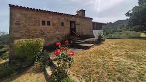 Un edificio de piedra con techo de tejas rojas, un pequeño porche y un jardín con flores rojas.