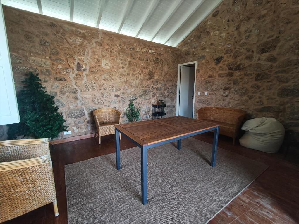 Una stanza con una parete in pietra, un tavolo di legno, due sedie in vimini, un piccolo albero di Natale e una porta.