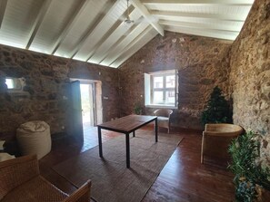 A rustic room with stone walls, a wooden ceiling, a table, chairs, and a window. - Quinta de Gonçalo  (Guarda)