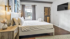 A bedroom with a bed, bedside table, lamp, artwork, curtains, and a television.