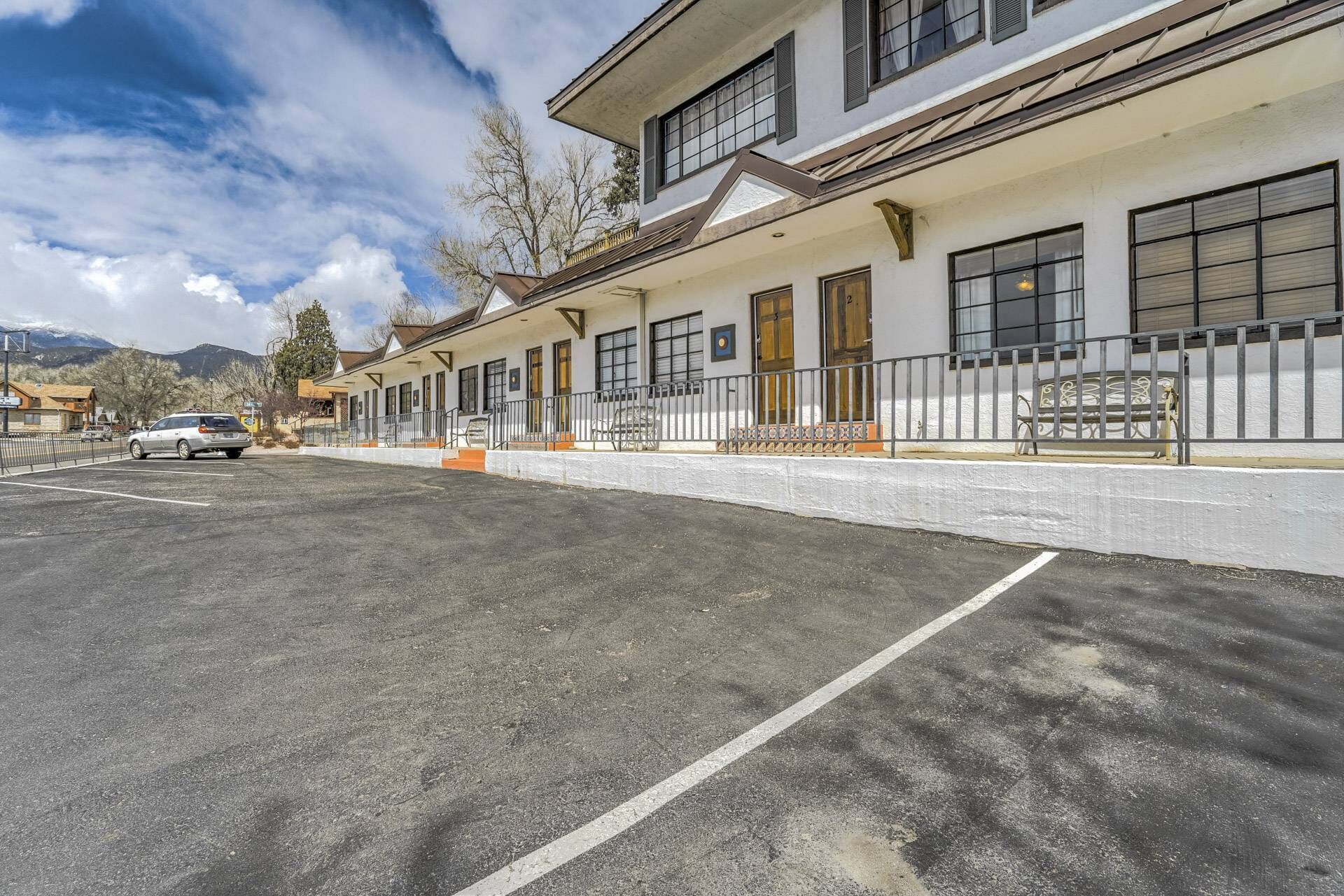 Un hotel con zona de estar cubierta al aire libre, aparcamiento y montañas al fondo.