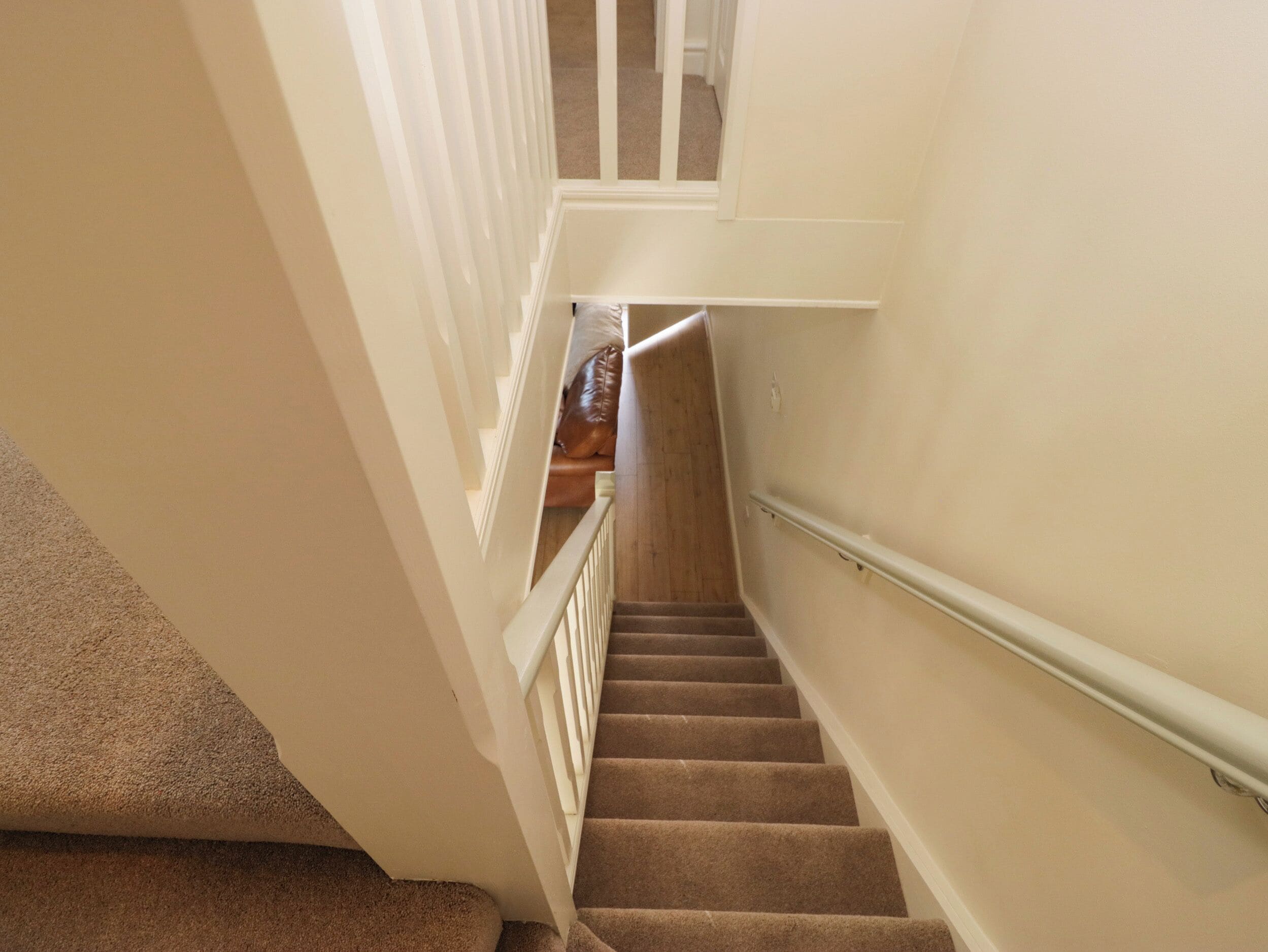 A carpeted staircase with a handrail, leading to a landing with a brown leather sofa.