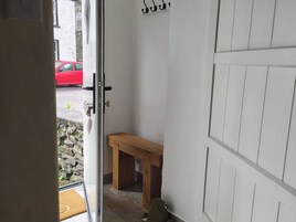Un vano de puerta que da a una habitación con un banco de madera, una pared de piedra y un coche rojo estacionado fuera.