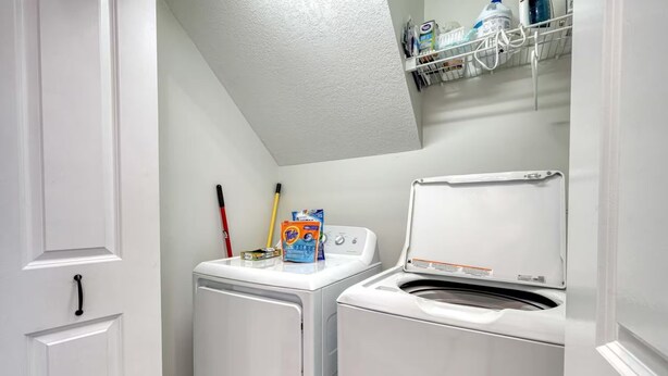 A laundry room with a washing machine and dryer, a shelf with cleaning supplies, and a door with a handle. - Cozy 3-bedroom entire home near wineries & waterfalls in Dahlonega, GA (Dahlonega)