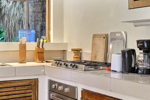 Een keuken met een gasfornuis, houten kastjes, een koffiezetapparaat en een raam met uitzicht op de omgeving.