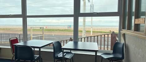 Una habitación con un ventanal grande que da a la playa y una valla. Hay una mesa con sillas y una butaca roja.