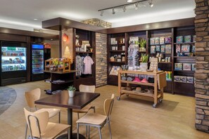 Un café avec un mur en pierre, des étagères remplies de divers objets, une table avec des chaises et un distributeur automatique.