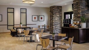 Een restaurantruimte in een hotel met verschillende tafels en stoelen, een accentmuur van steen, en een bar met keukenapparatuur.