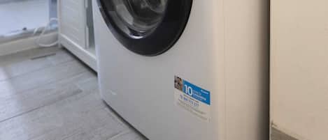 A front-loading washing machine in a modern bathroom with a shower area visible to the left.