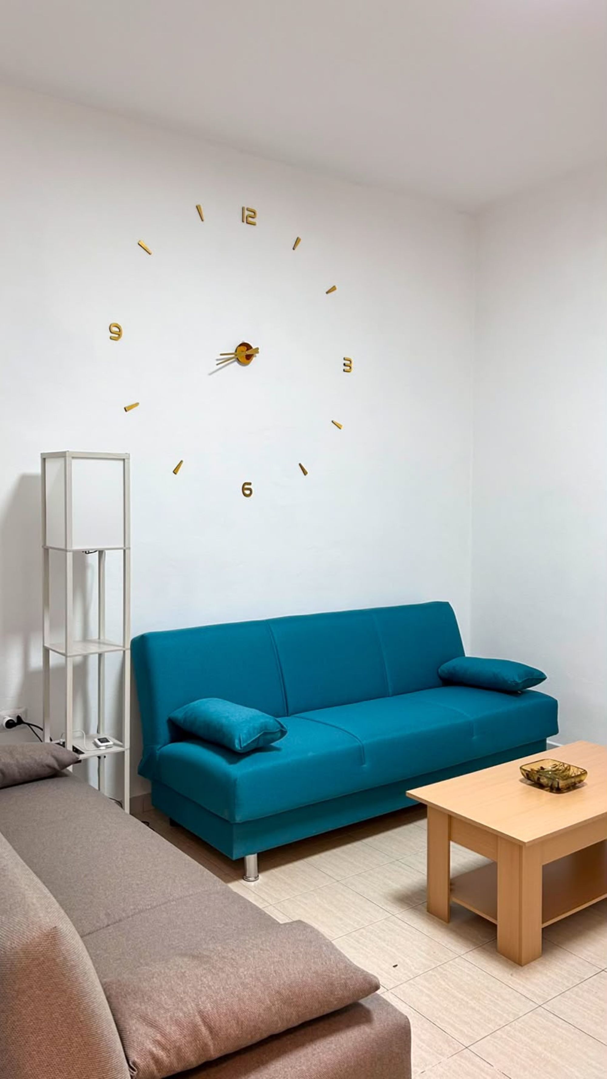 A modern living room with a blue sofa, a wooden coffee table, and a wall clock.