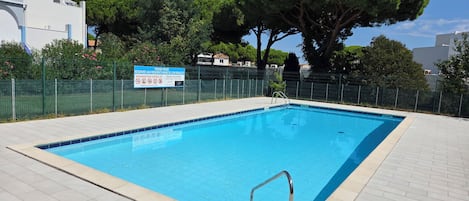 A swimming pool with a metal ladder, surrounded by a fence and trees.