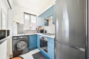 A compact kitchen with a washing machine, a stove, and a refrigerator. - Emerald Garden Suite - Wifi,parking,garden,sleep 2 (Croydon)