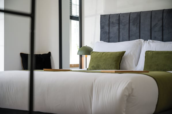 A neatly made bed with white and green pillows, a grey headboard, and a lamp on the nightstand. - Emerald Garden Suite - Wifi,parking,garden,sleep 2 (Croydon)