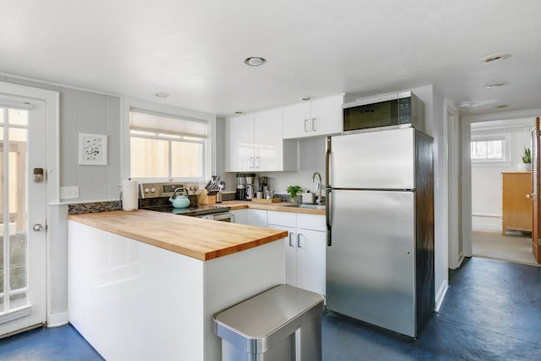A modern kitchen with white cabinetry, a stainless steel refrigerator, and a wooden countertop.