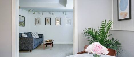 Una sala de estar con un sofá, una mesa de centro y un florero con flores. En la pared hay cuadros enmarcados.