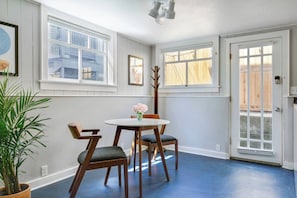 A room with a round table and two chairs, a potted plant, and a door leading outside.