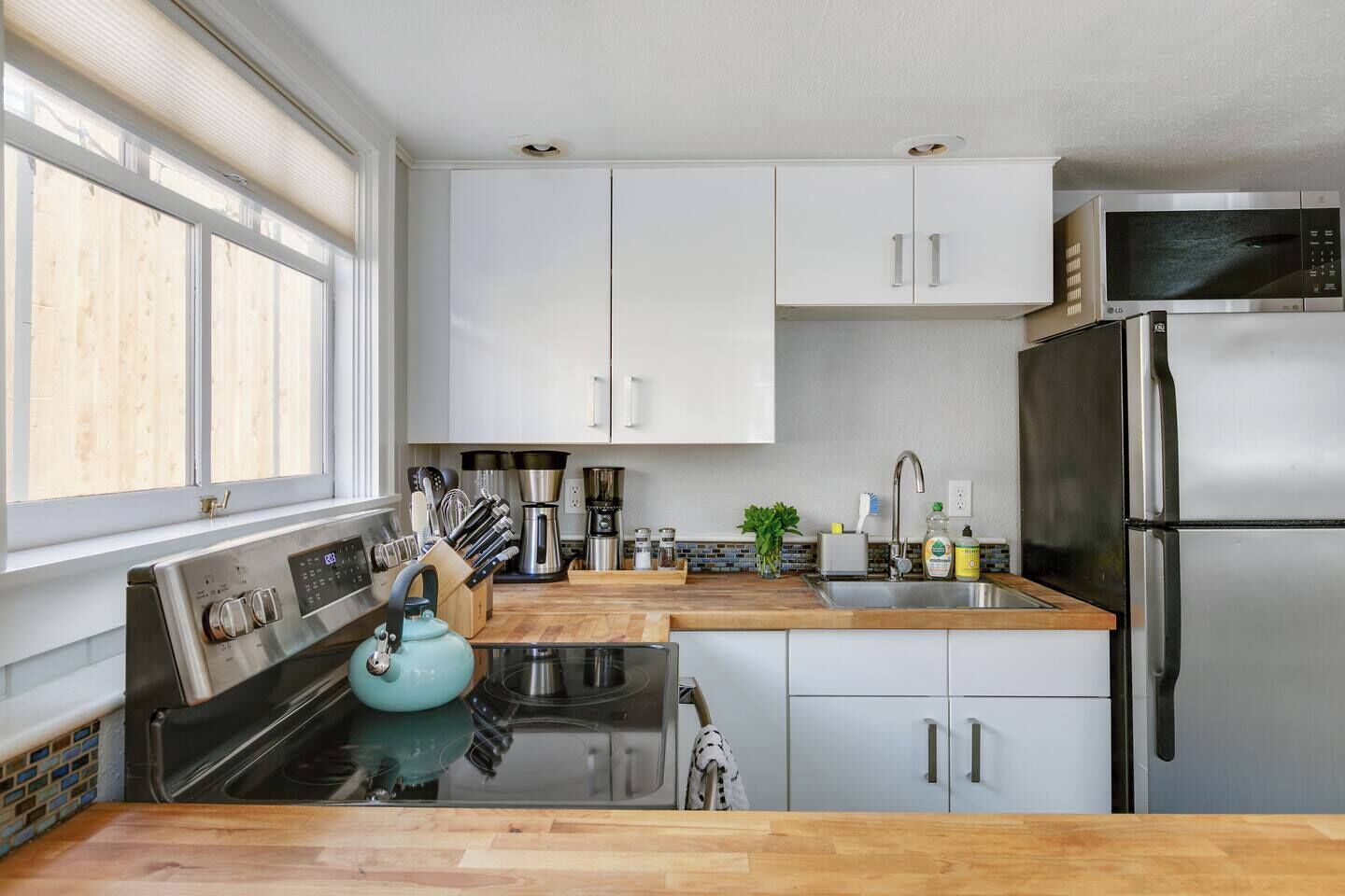 Una cucina moderna con mobili bianchi, elettrodomestici in acciaio inossidabile e un'ampia finestra che garantisce luce naturale.