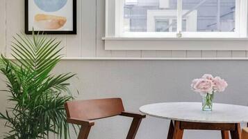 A room with a round table, a chair, a potted plant, and a framed artwork on the wall.