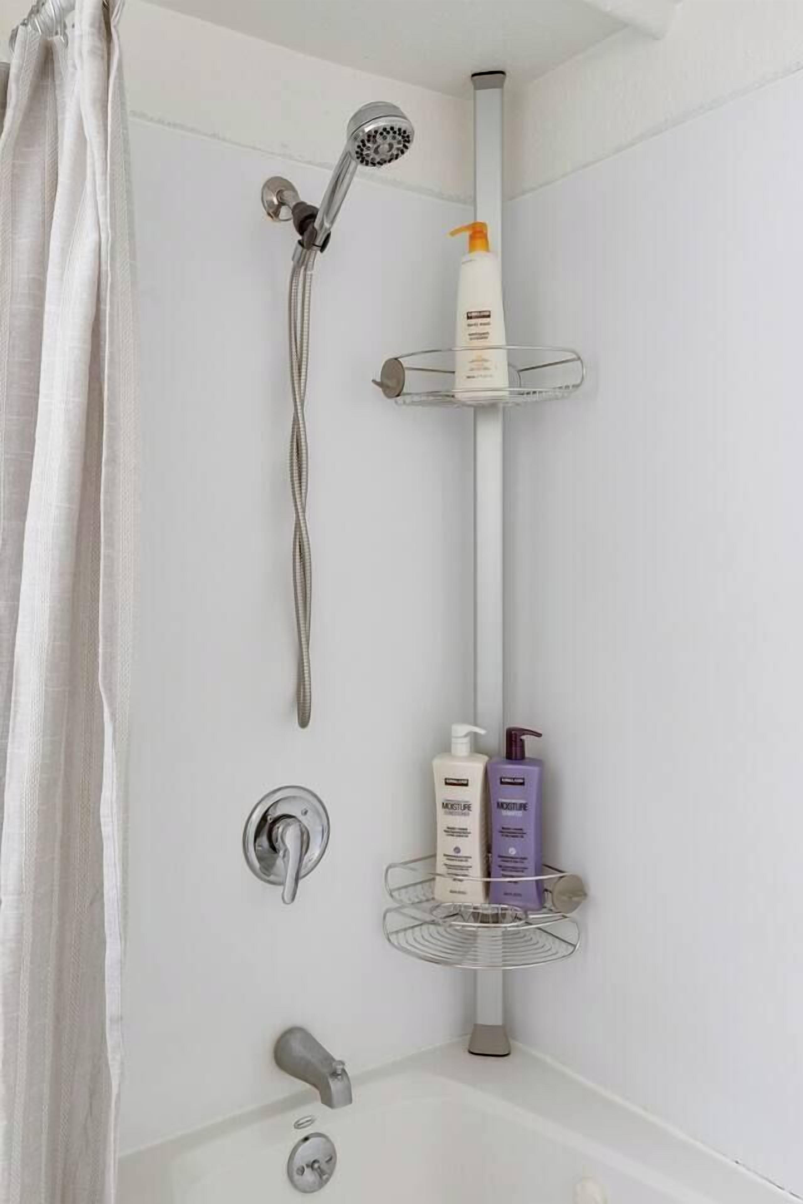 Un angolo doccia con soffione a mano, una bottiglia di shampoo e un erogatore di sapone.
