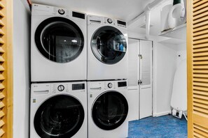 Un lavadero con cuatro lavadoras apiladas, una puerta blanca y un suelo azul.