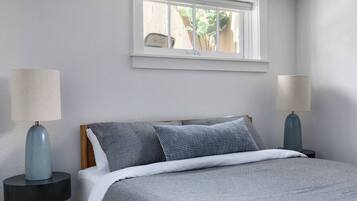 A bedroom with a bed, two bedside tables, a window, and a view of greenery outside.