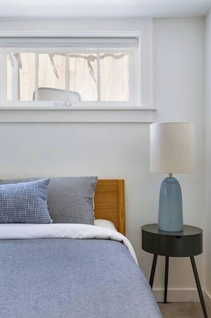 A bedroom with a bed, a nightstand, a lamp, and a window.