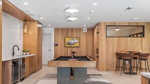 A modern kitchen with a pool table, wooden paneling, and a dining area with bar stools.