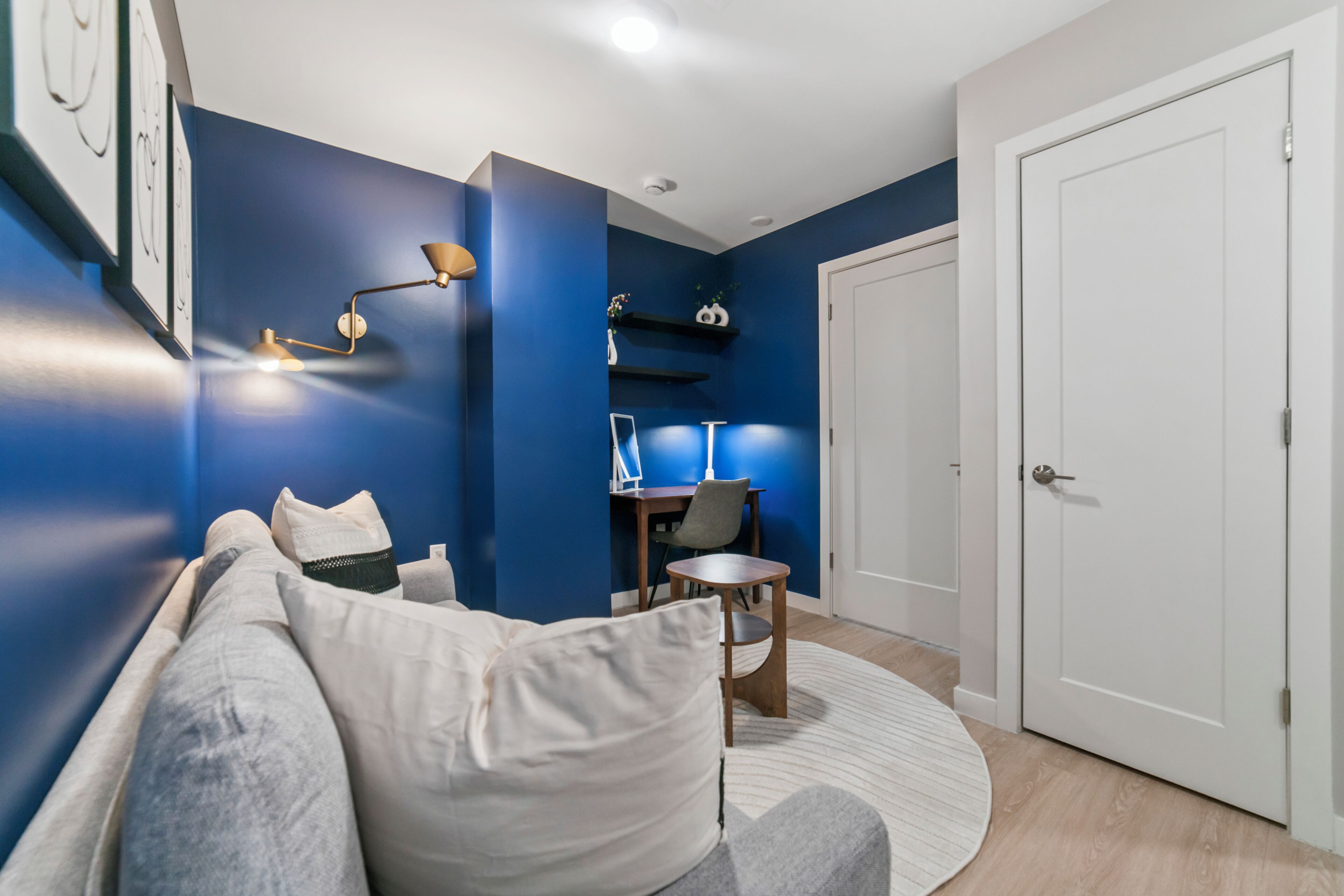 Una sala moderna con una pared azul de acento, un sofá gris, una mesita redonda y una puerta blanca.