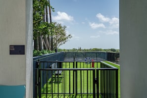 A view of a fenced outdoor area with a grassy field, a red fire hydrant, and a bench.