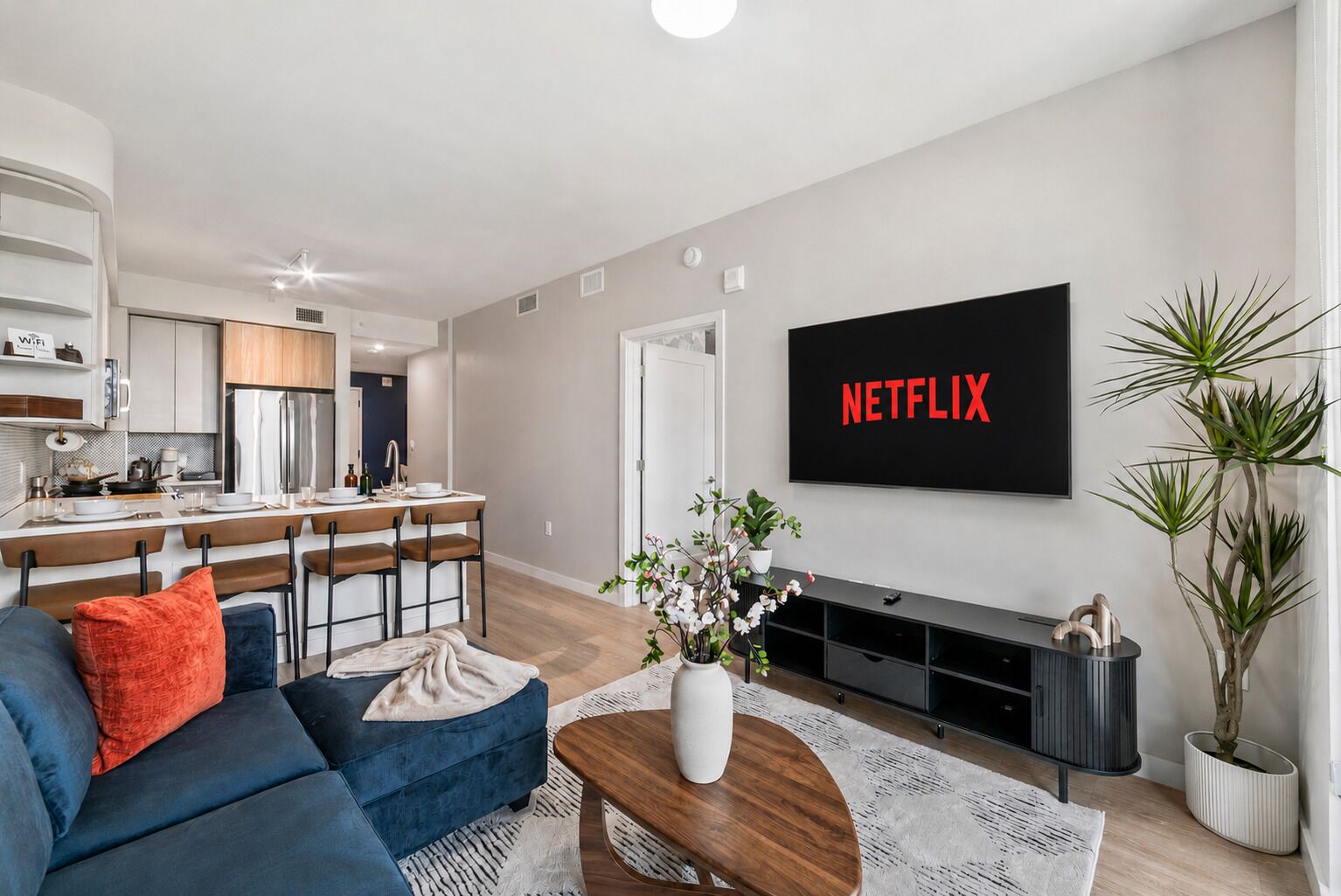 Uma sala de estar moderna com um sofá azul, uma mesa de centro e uma TV de tela plana exibindo 'NETFLIX'.