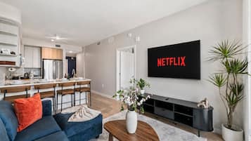 Uma sala de estar moderna com um sofá azul, uma mesa de centro e uma TV de tela plana exibindo 'NETFLIX'.