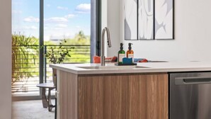 A modern kitchen with a large island, stainless steel appliances, and a view of a garden.