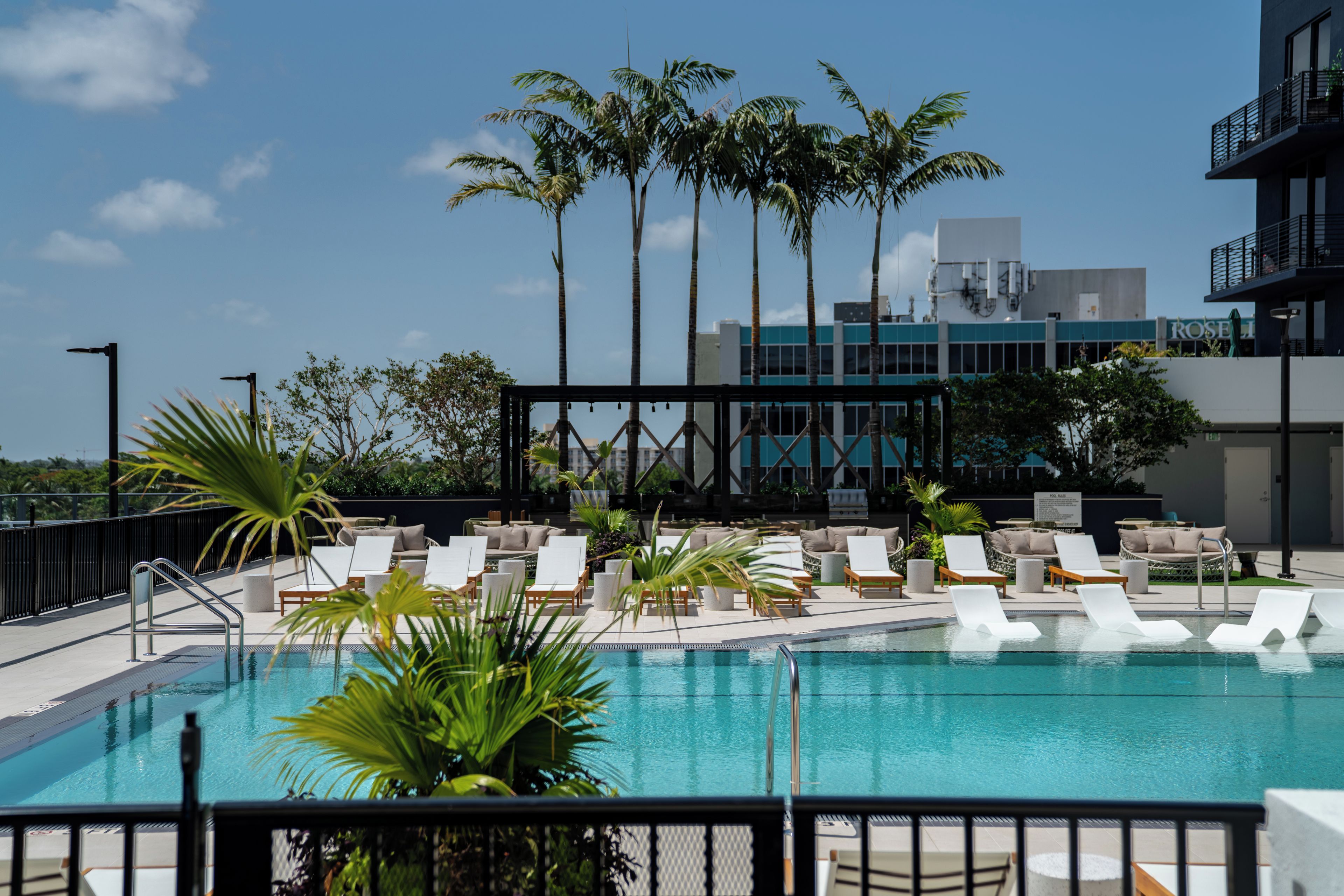A pool area with lounge chairs, palm trees, and a building in the background.
