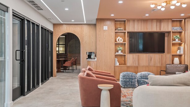 A modern living room with a flat-screen TV, wooden shelving, and comfortable seating.