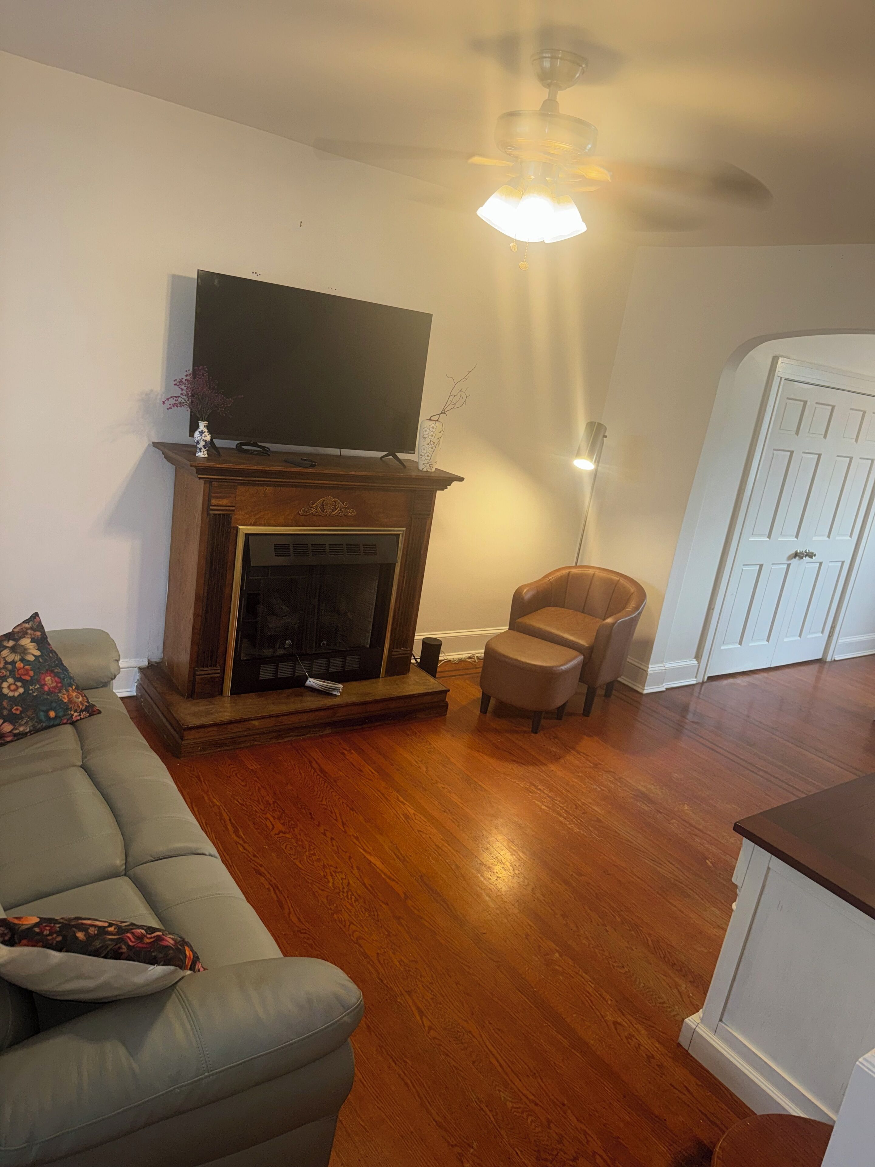 A living room with a fireplace, a television mounted above it, a sofa with cushions, a chair, and a door in the background.