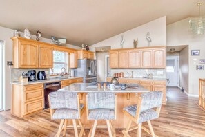 Una cocina amplia con armarios de madera, una isla central con taburetes de bar y un refrigerador de acero inoxidable.