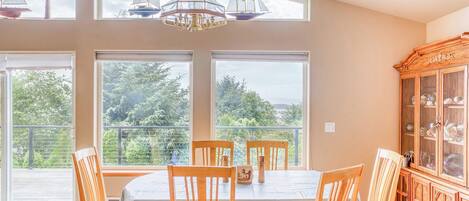 A dining room with a table and chairs, large windows, and a wooden cabinet with glass doors.