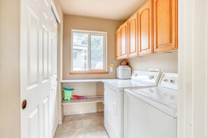 A laundry room with a washing machine, a dryer, wooden cabinets, a window, and a shelf with cleaning supplies.