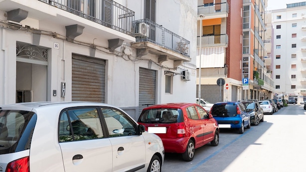 Fila de cotxes aparcats al costat d'un carrer amb edificis a banda i banda.