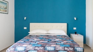 Un llit amb un estovat estampat, un panell de capçal blanc i una tauleta de nit amb un llibre i una tassa.