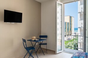A balcony with a view of buildings and the sea, a table with chairs, and a flat-screen TV mounted on the wall. - Alba Chiara Guest House - Sea View by BarbarHouse (Bari)