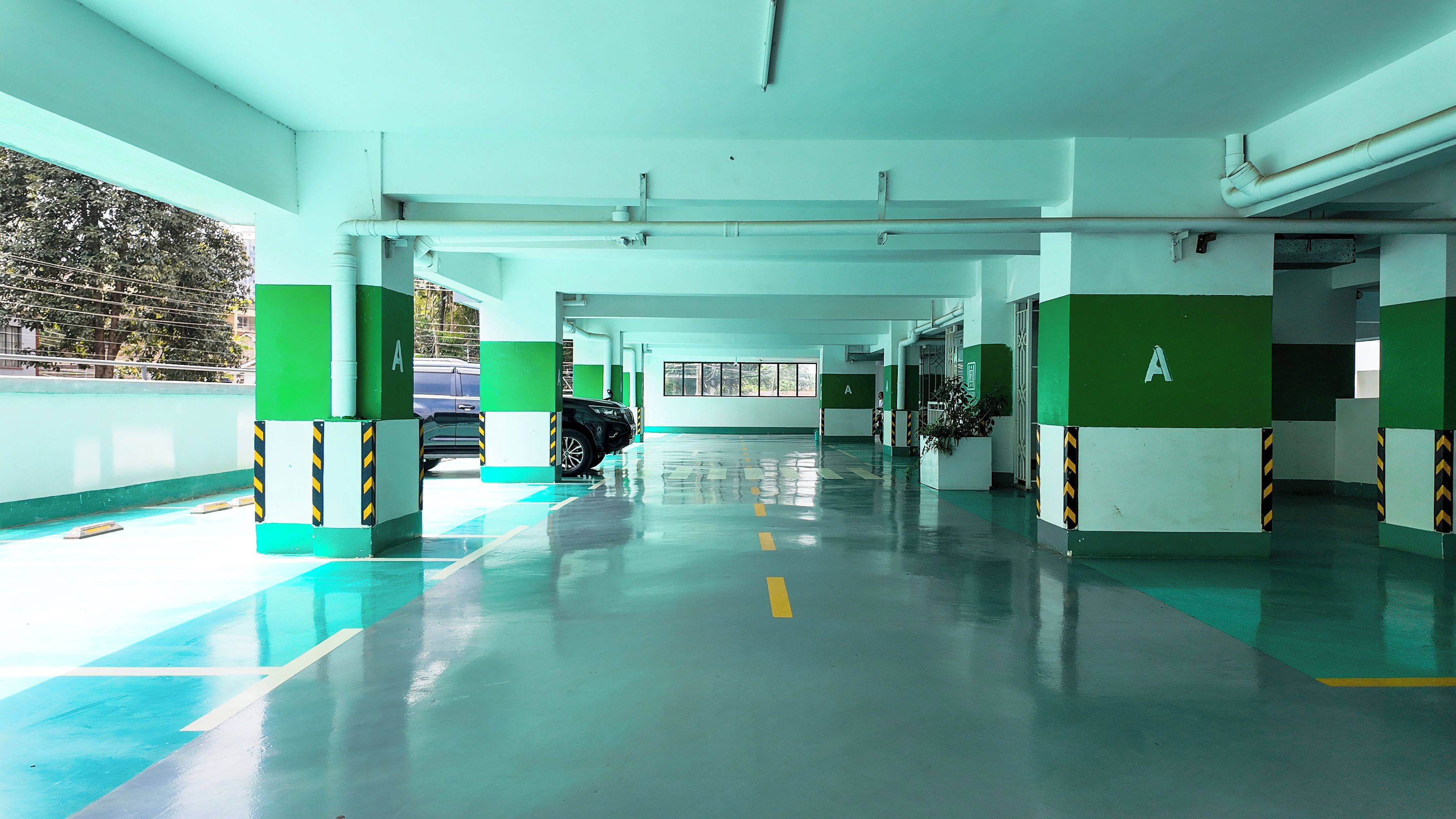A parking garage with green and white pillars, clear floor markings, and a car parked in the distance.