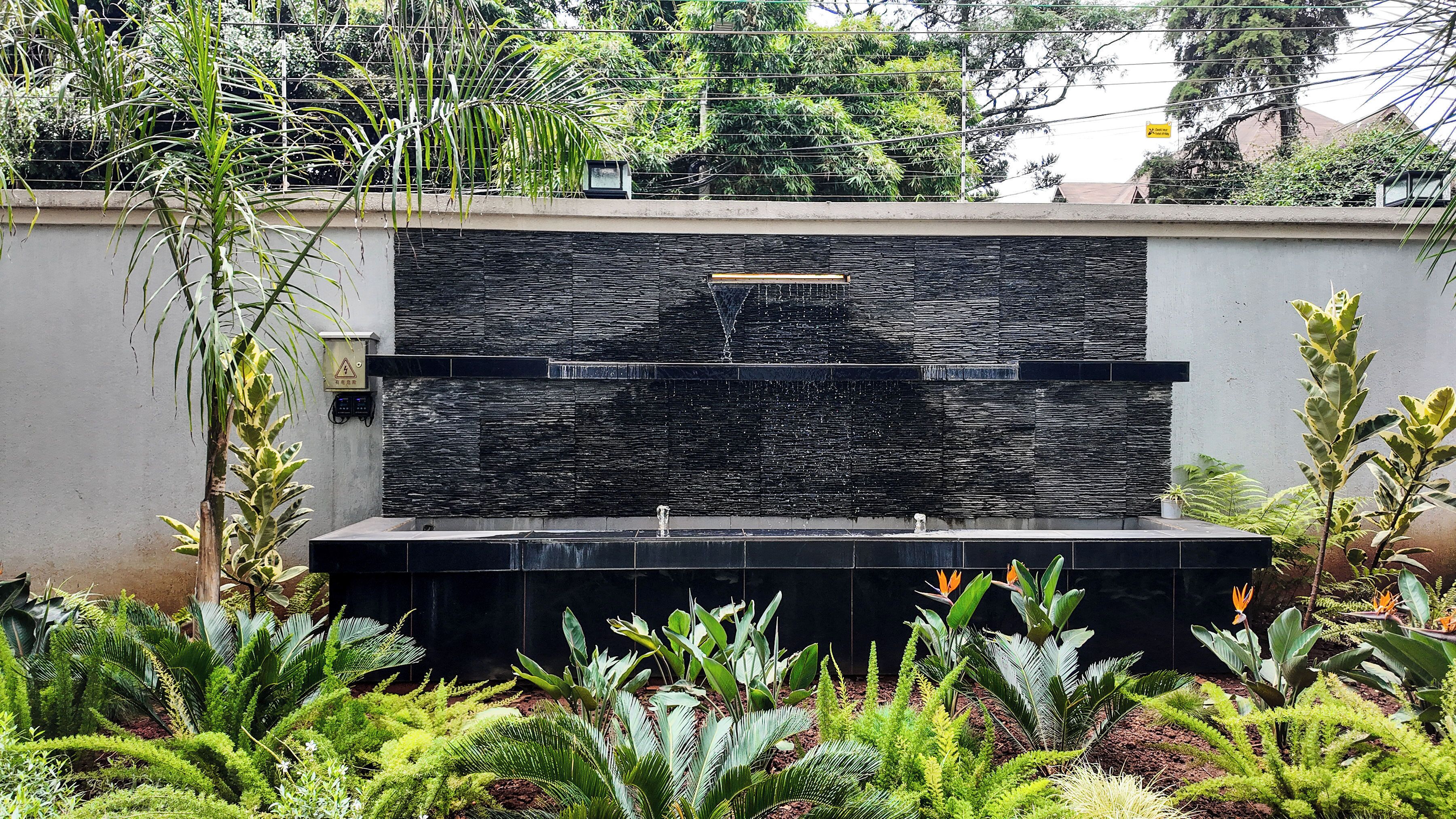 A modern outdoor water feature with a stone wall and a flat surface for water to cascade down.