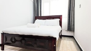 A neatly made bed with white linens in a room with a dark wooden headboard and a simple, clean design. - 2-bedroom apartment in beautiful Nairobi with fitness room access (Nairobi)